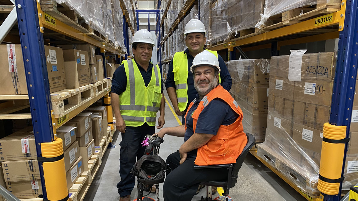 Rodrigo Caceres on his special wheelchair together with two colleagues in front of a high rack warehouse at the Grünenthal production site in Chile.