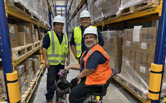 Rodrigo Caceres on his special wheelchair together with two colleagues in front of a high rack warehouse at the Grünenthal production site in Chile.